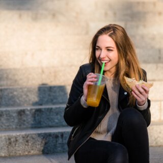 Ein Mädchen sitzt auf einer Stiege mit einem Saft und einem Sandwich in der Hand | © Shutterstock