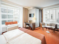 Junior Suite mit Wohn- und Schlafbereich mit großen Fenstern, die einen Blick auf die umliegenden Hochhäuser bieten im Hotel Europa Wien