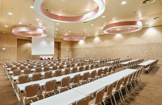 Geräumiger Seminarraum "Olympia Mancini 2" mit Bühne, breitem Rednerpult, zwei Beamern, einer großen Leinwand und großzügiger Saalbestuhlung | Austria Trend Hotel Savoyen
